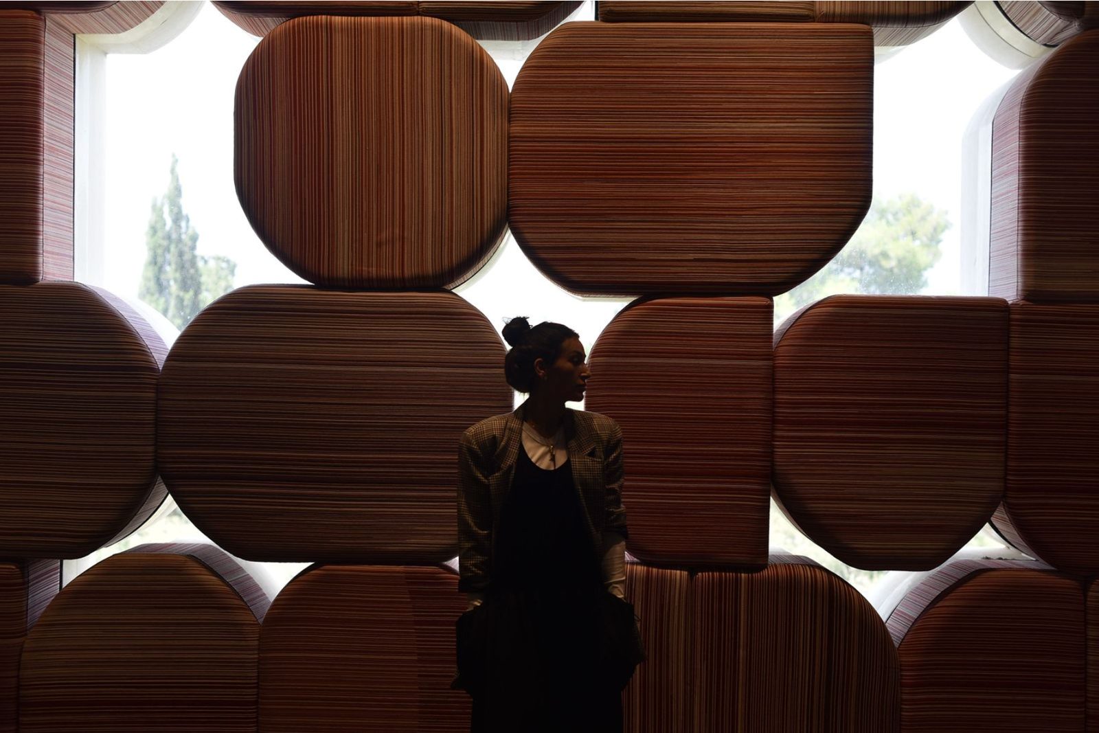 Tova Sherr silhouetted against a sculptural wall of warm wooden forms
